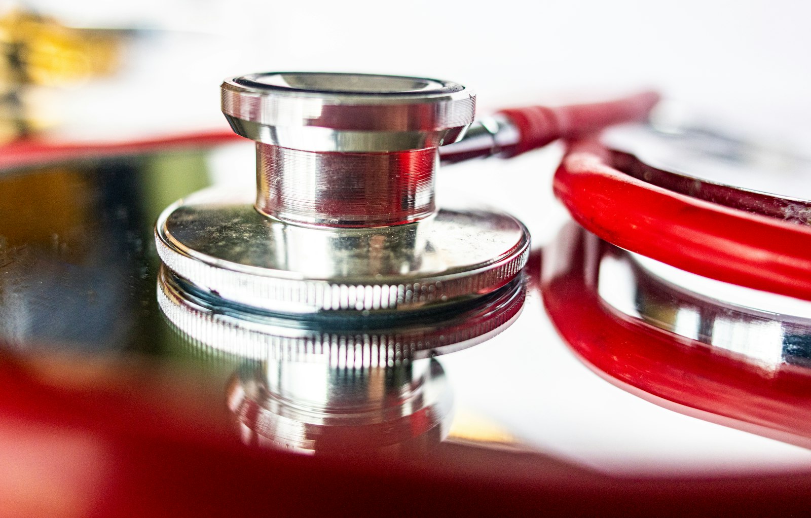 Close-up of a silver stethoscope chest piece with red tubing on a reflective surface