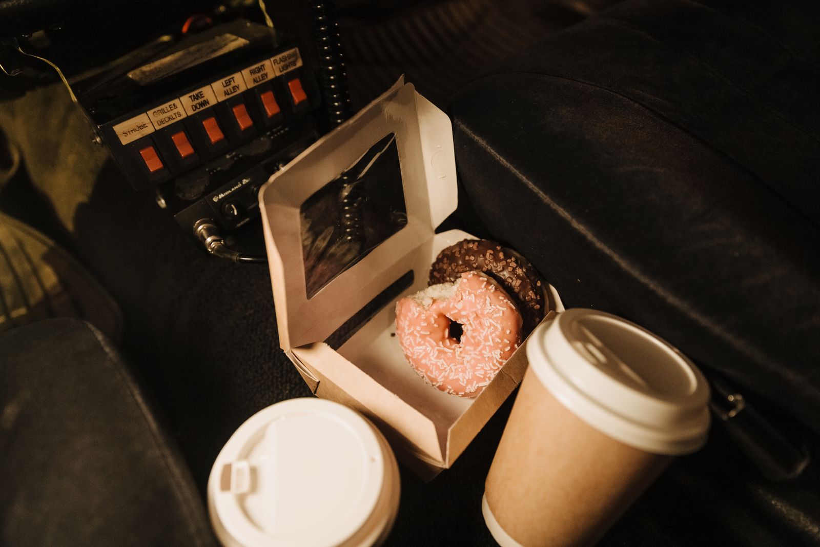 Open pastry box with a pink frosted donut beside two takeout coffee cups