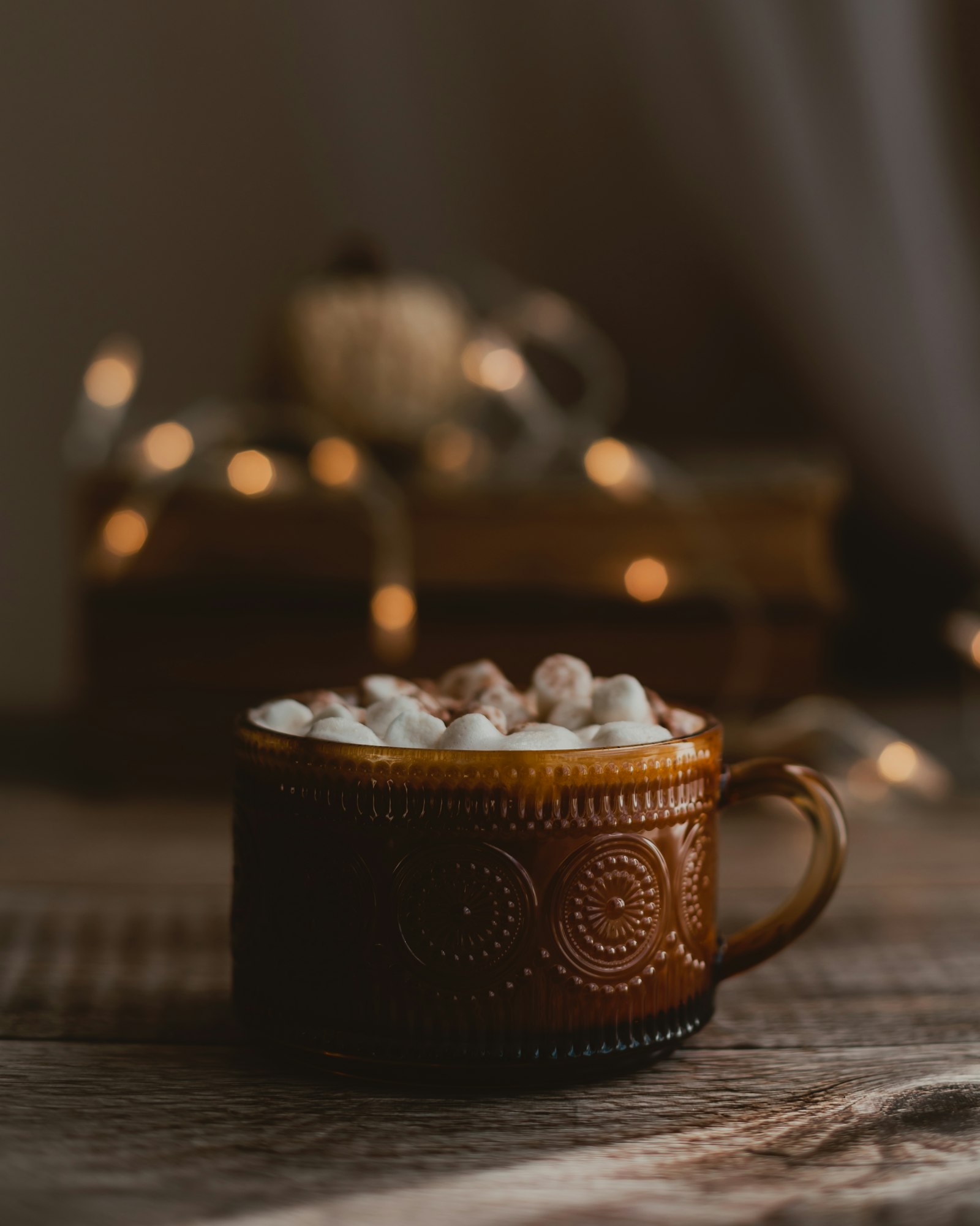 Mug of hot cocoa topped with mini marshmallows on a table with soft holiday lights in the background