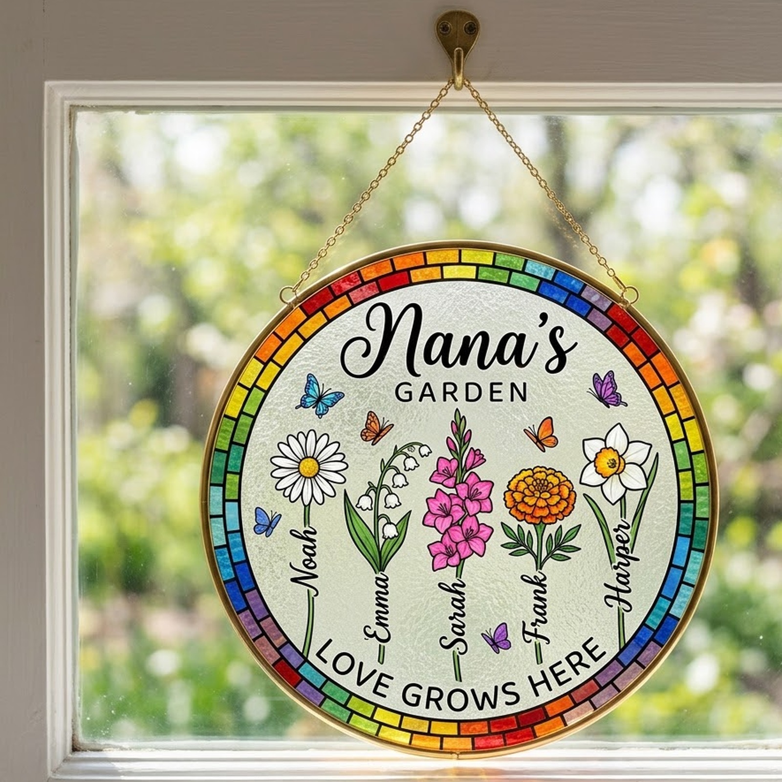 Nana's Garden Love Grows Here birth flower suncatcher hanging on a gold chain in a sunny window